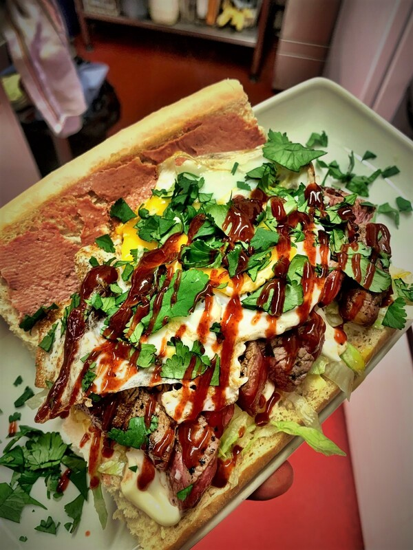 Filled baguette with grilled meat, lettuce, sauces and fresh herbs